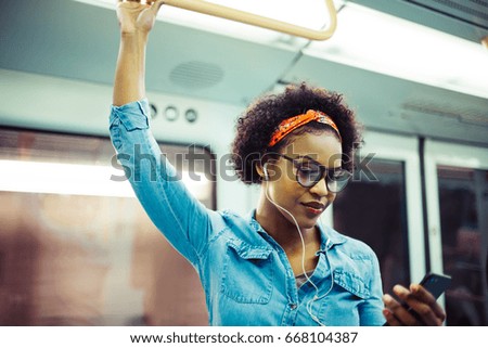 Smiling young African woman listening to music on her cellphone while standing on a subway train during her daily commute