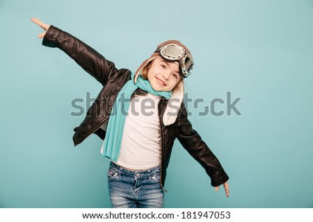 Beautiful smiling child (kid, girl) in helmet on a blue background playing with a plane. Vintage pilot (aviator) concept