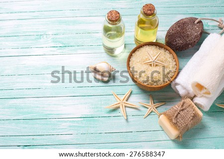 Spa or wellness setting. Sea salt in bowl, soap, aroma oil, pumice, towels and sea objects on turquoise painted wooden planks. Selective focus is on sea salt.