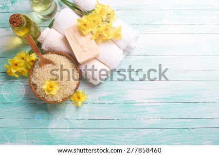 Spa or wellness setting. Natural sea salt in wooden bow, organic soap, aroma oil, towels and yellow flowers in ray of light on turquoise painted wooden background. Selective focus. Place for text.