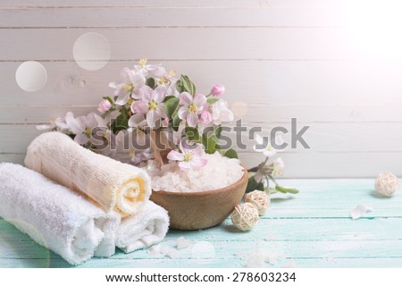 Spa or wellness setting. Sea salt in bowl, towels and apple blossom in ray of light on turquoise wooden background against white wall. Selective focus is on towels and salt. Place for text.