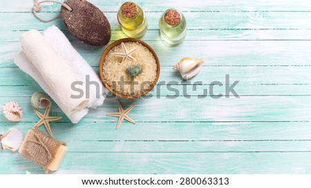 Spa or wellness setting. Sea salt in bowl, soap, aroma oil, pumice, towels and sea objects on turquoise painted wooden planks. Selective focus. Place for text. Toned image.