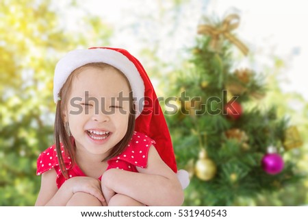 Little asian girl in santa hat smiling in front of Christmas tree