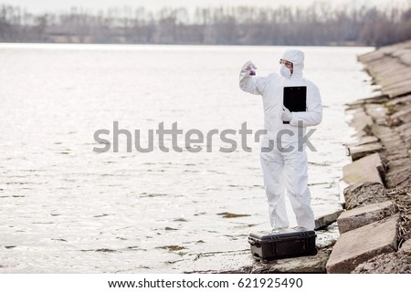 Scientist or biologist wearing protective uniforms examining the liquid contents of a test tube. Ecology and environmental pollution concept.