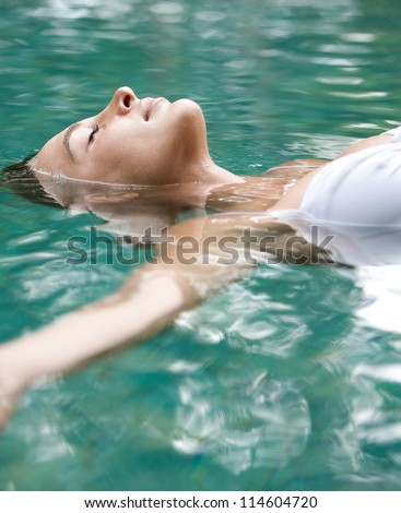 Close up view of an attractive young woman floating on a spa's swimming pool, smiling.