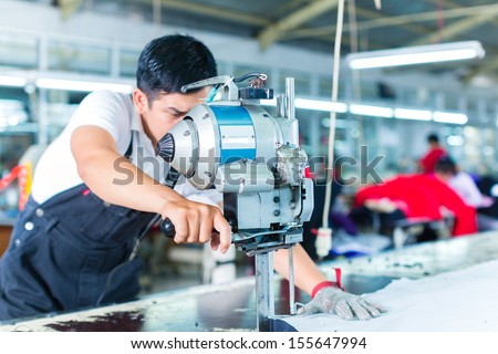 Indonesian worker using a cutter - a large machine for cutting fabrics - in a asian textile factory, he wears a chain glove