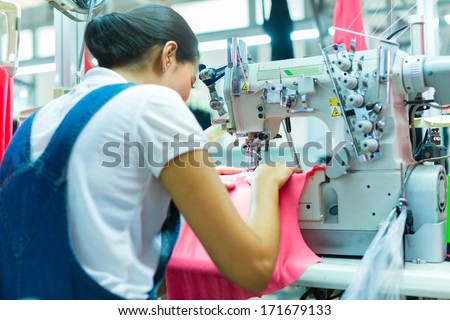 Asian Seamstress or worker in an Asian textile factory sewing with a industrial sewing machine, she is very accurate