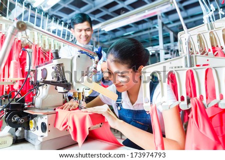 Asian Seamstress or worker in a textile factory sewing with a industrial sewing machine, she is very accurate, the manager looking pleased at her work