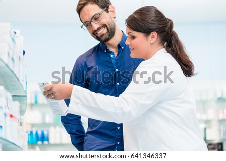 Pharmacist talking to customer in drug store, woman and man standing in front of shelves