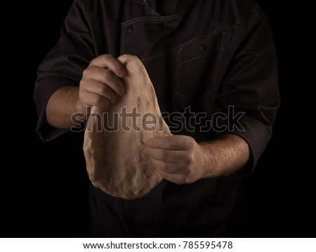 Hands of the Baker knead layer of dough, isolated on black background
