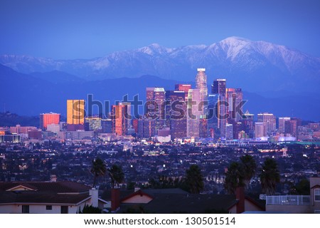 Downtown Los Angeles skyline over snowy mountains at twilight.