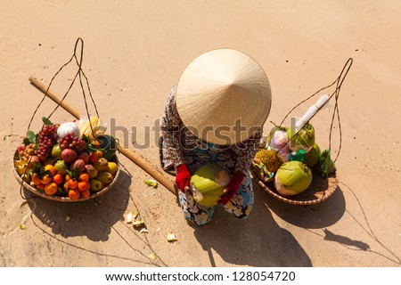 Vietnamese woman in a straw hat on the beach selling fruit and reveals the coconut