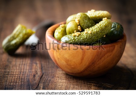 Pickled cucumbers in a wooden bowl with mustard seeds against dark rustic background