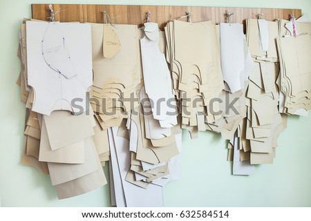 Many paper brown patterns for sewing clothes for babies and newborns of different sizes hanging on wall in sewing factory interior. Horizontal color photo.