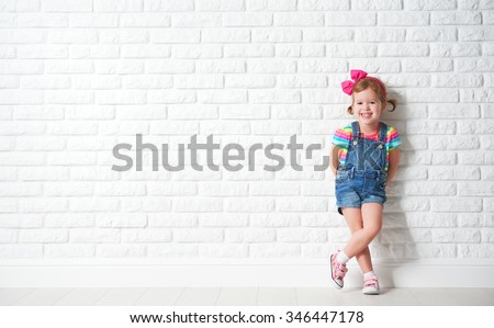 Happy child little girl laughing at a blank empty brick wall