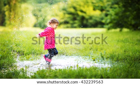 happy child girl running and jumping in puddles after rain in summer