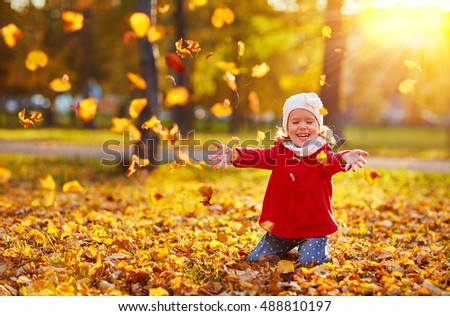 happy child girl laughing and playing leaves in autumn outdoors