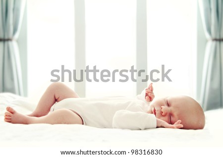 Newborn baby sleeping on white blanket in front of a window. Soft focus, very shallow DOF.