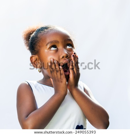 Portrait of surprised little African girl with hands on face looking up.Isolated against light background.