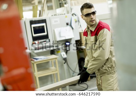 Craftsman wearing working clothes and protective eyewear woodworking in furniture industry operating on machine