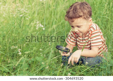 Happy little boy exploring nature with magnifying glass at the day time