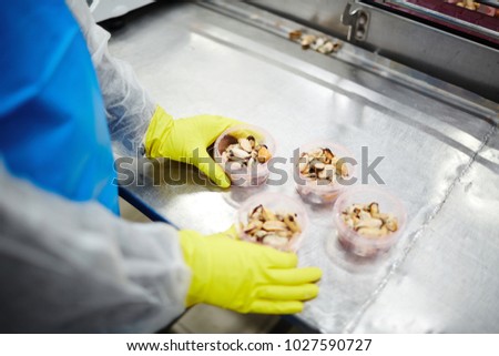 Staff packing processed mussels in plastic containers while working in seafood production factory