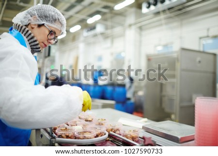 Young staff sorting seafood into plastic containers while standing by processing line in factory