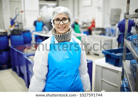 Smiling female in protective uniform looking at camera in fish processing department