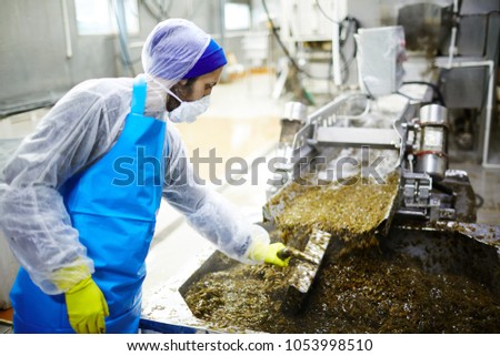 Seafood factory staff standing by production line and mixing seaweed salad in huge container with special handtool