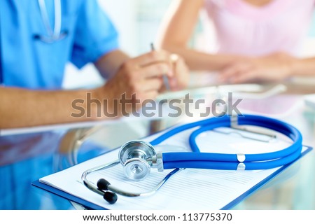 Close-up of stethoscope and paper on background of doctor and patient hands