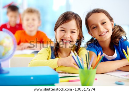 Portrait of two diligent girls looking at camera at workplace with schoolboys on background