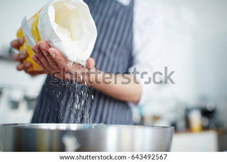Baker adding flour in bowl to make dough