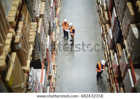Above view of warehouse workers group in aisle between rows of tall shelves full of packed boxes and goods