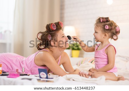 Mom and daughter in the bedroom on the bed in the curlers make up, paint their nails and have fun