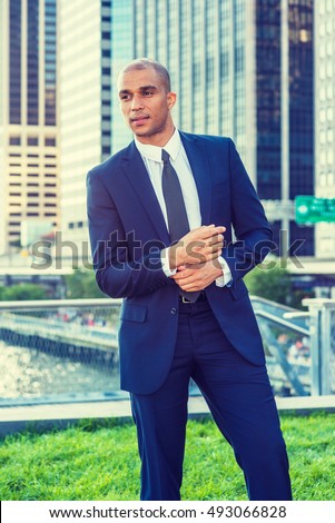 Portrait of Young European Businessman in New York. Wearing blue suit, white shirt, black tie, Mixed Race French guy with shaved head stands in business district, hand touching cuff, going to work.