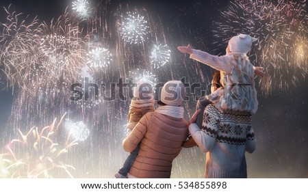 New Year holiday. Happy family, parents and daughters children girls are watching fireworks. The child sits on the shoulders of his father on snowy winter walk in nature. Holidays winter season.