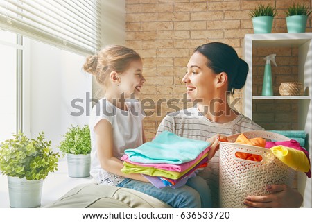 Beautiful young woman and child girl little helper are having fun and smiling while doing laundry at home.