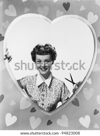 Woman looking through heart shape with scissors