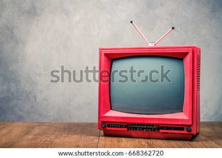 Retro old red TV receiver on table front textured concrete wall background. Broadcasting concept. Vintage style filtered photo
