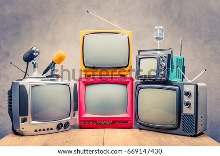 Retro old TV set receivers and microphones on table front textured concrete wall background. Broadcasting concept. Vintage style filtered photo