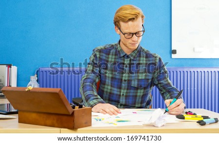 Young cartoonist at work, coloring sketches and drawings behind his desk