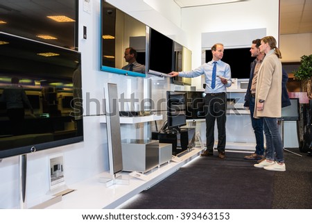 Salesman showing flat screen TV to young couple in electronics store