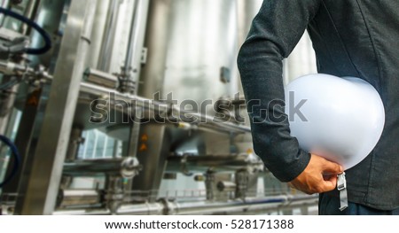 engineer suit white helmet for security stood on the details of shiny stainless steel pipes, tanks for the food industry.