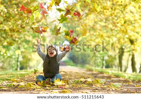 happy laughing kid throwing autumn fall leaves in an autumn alley