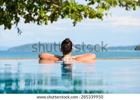 Relax and spa concept. Woman with a flower in hair relaxing in a pool towards the sea at Krabi, Thailand.