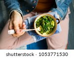 Small photo of Young woman holds in hands healthy seaweed chuka salad with greens, turnip, rocket salad, spinach, radish, dill, onion sprouts, oil. With legs and carpet. Top view. Raw, vegan, vegetarian food