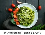 Zucchini raw vegan pasta with avocado dip sauce, spinach leaves and cherry tomatoes on plate. On dark background. Vegetarian healthy food