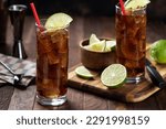 Rum and cola cocktail in tall glasses with lime slice on rustic wooden table