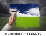 Man hand holding painting brush, paint bright day with blue sky and white cloud on green grass field replace bad cloudy day. Conceptual illustration of new better world or optimistic vision.