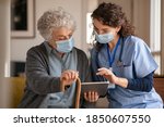 Small photo of Doctor and senior woman going through medical record on digital tablet during home visit wearing face mask. Old woman with nurse with surgical mask and using digital tablet during coronavirus pandemic